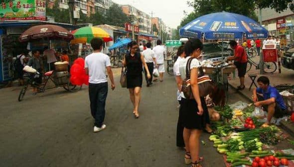 People shopping at a street market with various vegetables displayed on the ground. - Olive Oil Times