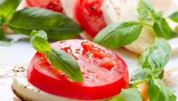 Sliced tomatoes and mozzarella cheese garnished with fresh basil leaves on a plate. - Olive Oil Times