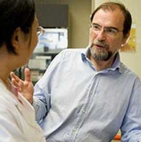 Two individuals, one wearing a white lab coat, engaged in a conversation in a laboratory environment. - Olive Oil Times