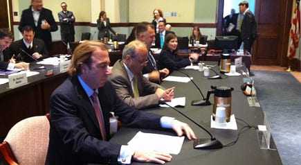 A group of individuals seated at a conference table during a meeting with documents and a coffee pot visible. - Olive Oil Times