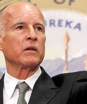 Man in a gray suit pointing while speaking at a podium with a seal in the background. - Olive Oil Times