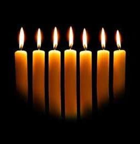 Eight yellow candles arranged in a row, each with a flame, against a dark background. - Olive Oil Times