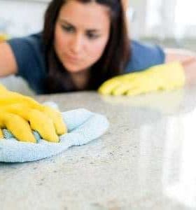 Individual wearing yellow gloves cleaning a countertop with a blue cloth in a bright indoor setting. - Olive Oil Times