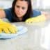 Individual wearing yellow gloves cleaning a countertop with a blue cloth in a bright indoor setting. - Olive Oil Times