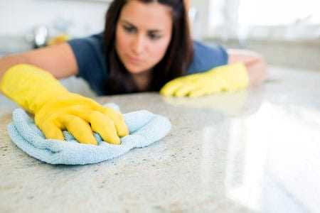 Individual wearing yellow gloves cleaning a countertop with a blue cloth in a bright indoor setting. - Olive Oil Times