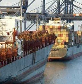 Two cargo ships docked at a port with containers stacked on their decks. - Olive Oil Times