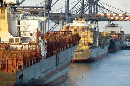 Two cargo ships docked at a port with containers stacked on their decks. - Olive Oil Times