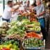 Vendors and customers interacting at a fresh produce market with various vegetables displayed. - Olive Oil Times