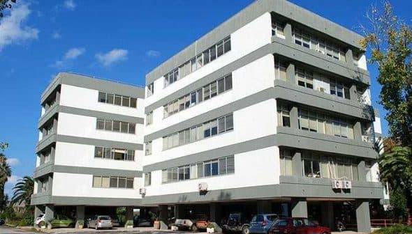 A multi-story office building featuring a modern architectural design with large windows and a gray and white color scheme. - Olive Oil Times