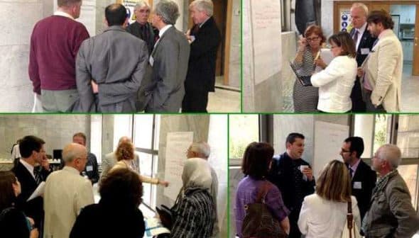 A group of people engaged in discussion during an international meeting, with papers and notes visible. - Olive Oil Times