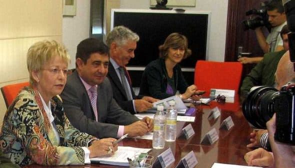 Group of individuals seated at a conference table during a meeting, with documents and water bottles present. - Olive Oil Times