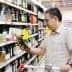 Man holding a bottle of olive oil while shopping in a grocery store aisle. - Olive Oil Times