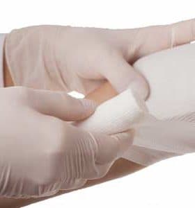 A medical professional in gloves applying a bandage to a patient's arm. - Olive Oil Times