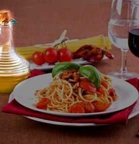 Plate of spaghetti topped with tomatoes and basil, accompanied by a cruet of olive oil and glasses of water and red wine. - Olive Oil Times