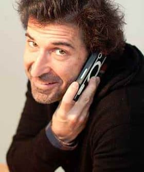 Man with curly hair holding a mobile phone to his ear while smiling. - Olive Oil Times