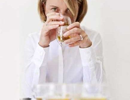 Woman holding a glass of olive oil while tasting it, with several glasses in front of her. - Olive Oil Times
