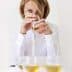 Woman holding a glass of olive oil while tasting it, with several glasses in front of her. - Olive Oil Times