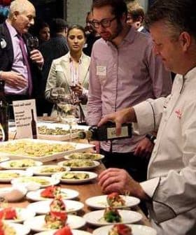 Chef pouring olive oil over a plate of food at a culinary event with attendees observing. - Olive Oil Times