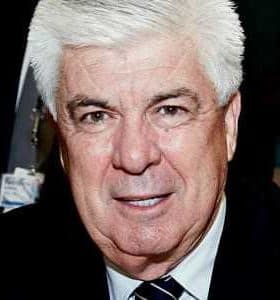 A man with white hair wearing a dark suit and tie, looking directly at the camera. - Olive Oil Times