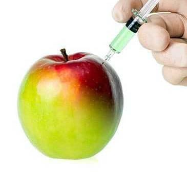 A red and green apple being injected with a syringe containing a green liquid. - Olive Oil Times