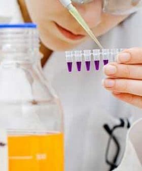 Laboratory technician using a pipette to transfer liquid into multiple test tubes in a lab setting. - Olive Oil Times