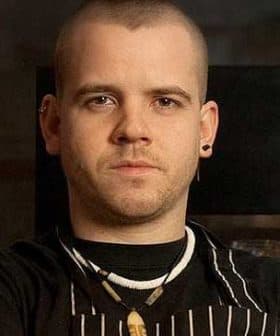 Man with short hair wearing an apron and necklace, looking directly at the camera. - Olive Oil Times