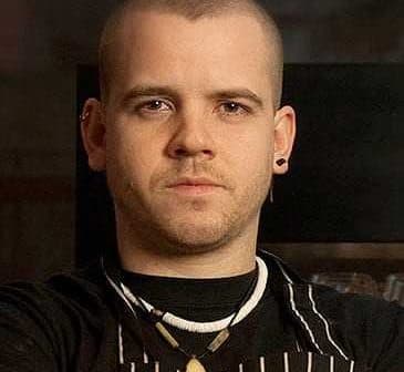 Man with short hair wearing an apron and necklace, looking directly at the camera. - Olive Oil Times