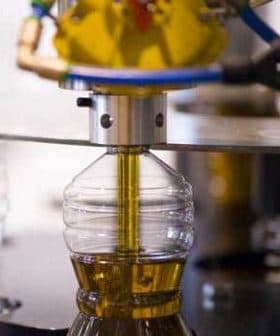 Machine filling a plastic bottle with olive oil during the bottling process. - Olive Oil Times