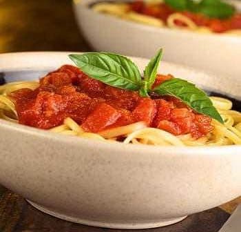 Bowl of spaghetti topped with tomato sauce and fresh basil leaves. - Olive Oil Times