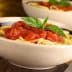 Bowl of spaghetti topped with tomato sauce and fresh basil leaves. - Olive Oil Times