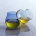 Two glass containers with olive oil, one blue and one clear, positioned on a reflective surface. - Olive Oil Times