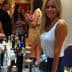 Woman with long blonde hair standing at a table filled with various product bottles at an event. - Olive Oil Times
