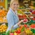 Woman in a gray blazer holding a red apple while carrying a basket of fresh fruits and vegetables. - Olive Oil Times