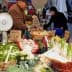 A vendor weighing vegetables at a market stall with various fresh produce displayed. - Olive Oil Times