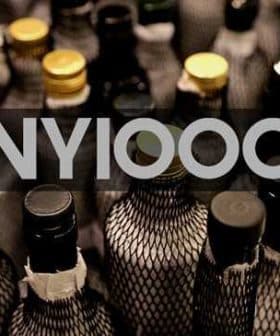 Multiple bottles with dark netting and various colored caps arranged closely together. - Olive Oil Times