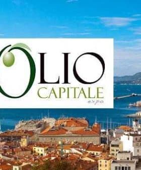 Logo of Olio Capitale Expo displayed over a coastal city view with boats and buildings. - Olive Oil Times