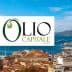 Logo of Olio Capitale Expo displayed over a coastal city view with boats and buildings. - Olive Oil Times