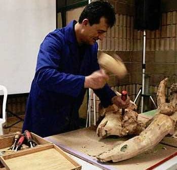 A woodworker using a chisel and hammer to carve a wooden sculpture during a demonstration. - Olive Oil Times