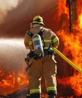 Firefighter in protective gear using a hose to spray water on a large fire. - Olive Oil Times
