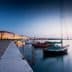 Several boats docked at a harbor with calm water during twilight hours. - Olive Oil Times