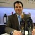 A man in a suit sitting at a table with two bottles of olive oil in front of him. - Olive Oil Times