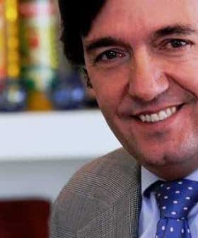 A man wearing a suit and a polka dot tie smiling at the camera. - Olive Oil Times