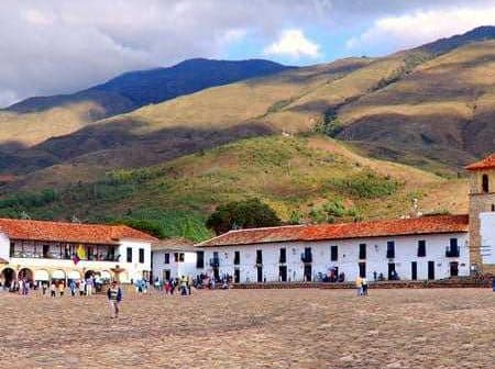 Colonial buildings with red roofs and cobblestone plaza in a mountainous region of Colombia. - Olive Oil Times