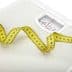 White analog bathroom scale with a measuring tape curled around it. - Olive Oil Times