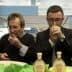 Two men tasting olive oil from small cups at an event, focusing on the aroma and flavor. - Olive Oil Times