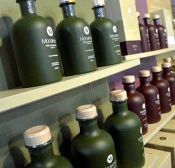 Various olive oil bottles in green and brown glass with wooden caps arranged on a shelf. - Olive Oil Times