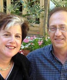Two individuals smiling while posing for a photograph outdoors, with plants in the background. - Olive Oil Times