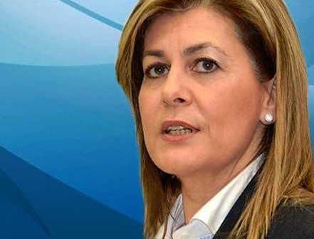 Woman with light brown hair wearing a dark blazer and white shirt against a blue background. - Olive Oil Times