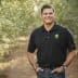 Man wearing a black polo shirt and jeans standing in an olive grove with trees in the background. - Olive Oil Times