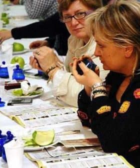 Two women participating in an olive oil tasting event, examining samples at a table. - Olive Oil Times